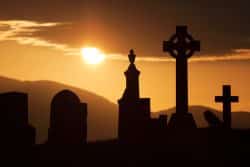 A cemetery with Irish crosses silhouetted against the sun.