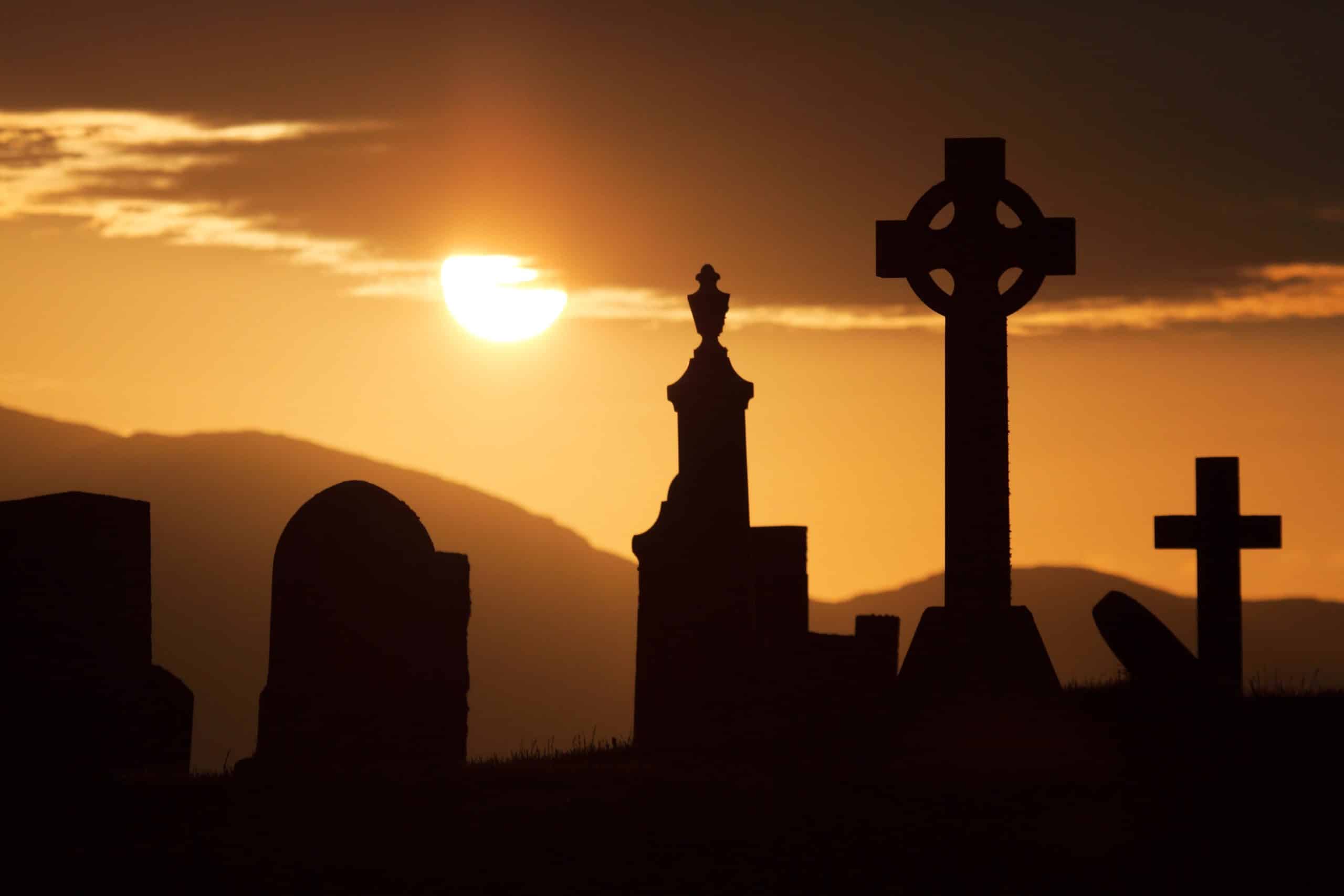 A cemetery with Irish crosses silhouetted against the sun.