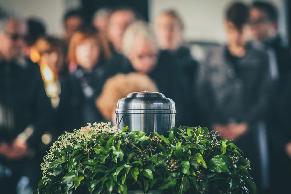 An urn in a wreath in front of a crowd of mourners who are out of focus.