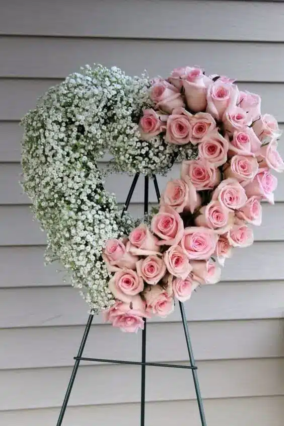 A heart-shaped wreath on an easel comprised of two different color flowers.