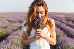 A young woman in a flower field holding a bouquet up to her nose to smell it.