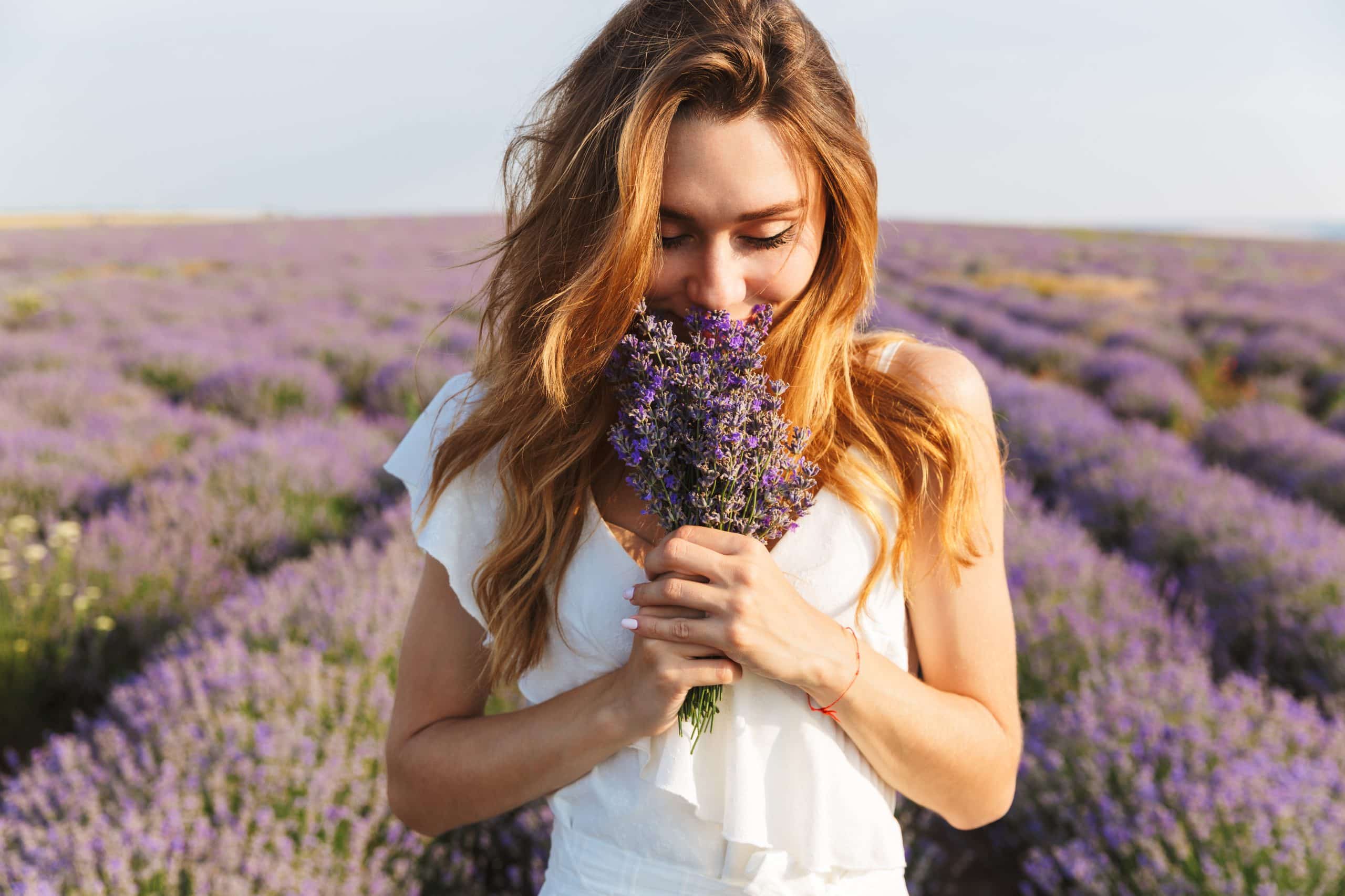 A young woman in a flower field holding a bouquet up to her nose to smell it.