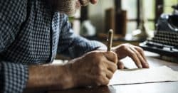 Man bent over a desk handwriting a letter on white paper.