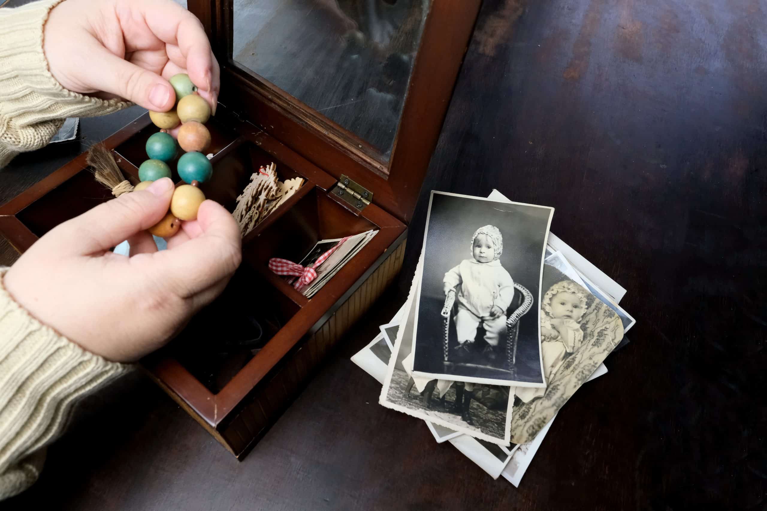 A pair of woman's hands sorting through a box of photographs and other family treasures.