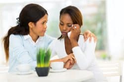 One woman comforts another at a table.