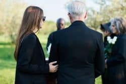 Well-appointed man and a woman attending a funeral, facing away from the camera.
