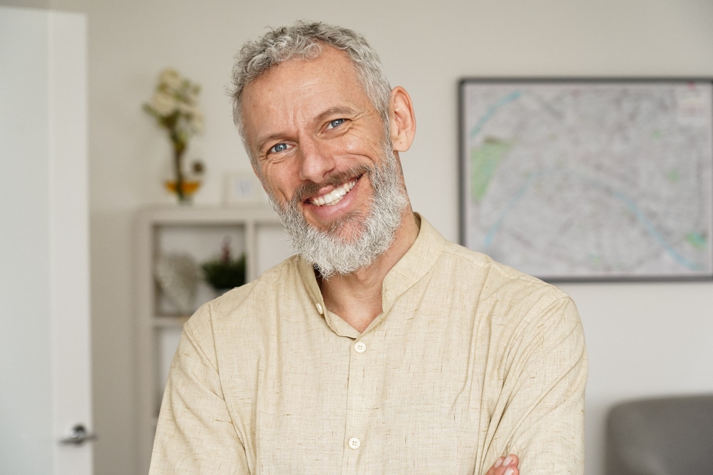 A healthy older man with gray hair and beard smiling in the direction of the camera.