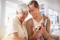 An older woman embraces a younger adult woman who is holding a string of pearls and a jewelry box.