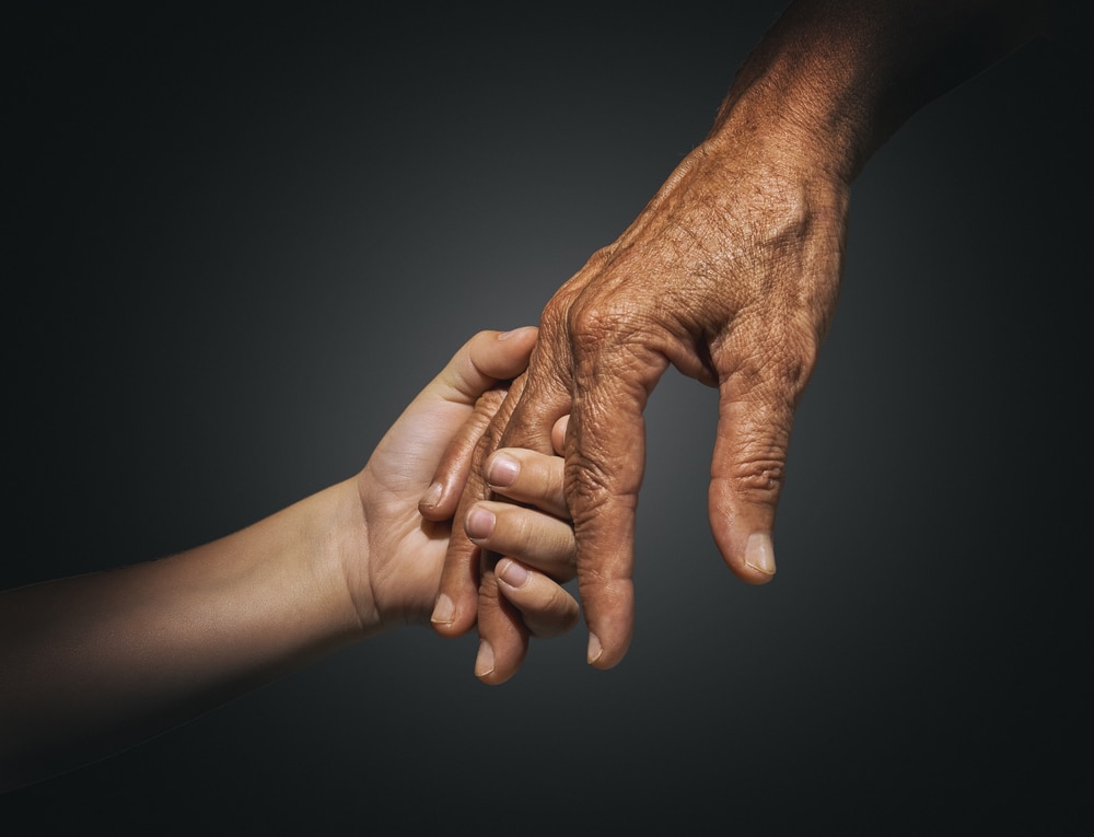 A child's hand grasps the fingers of an older hand.