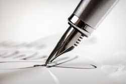 A black and white image of the head of a fountain pen writing in cursive on a piece of paper.