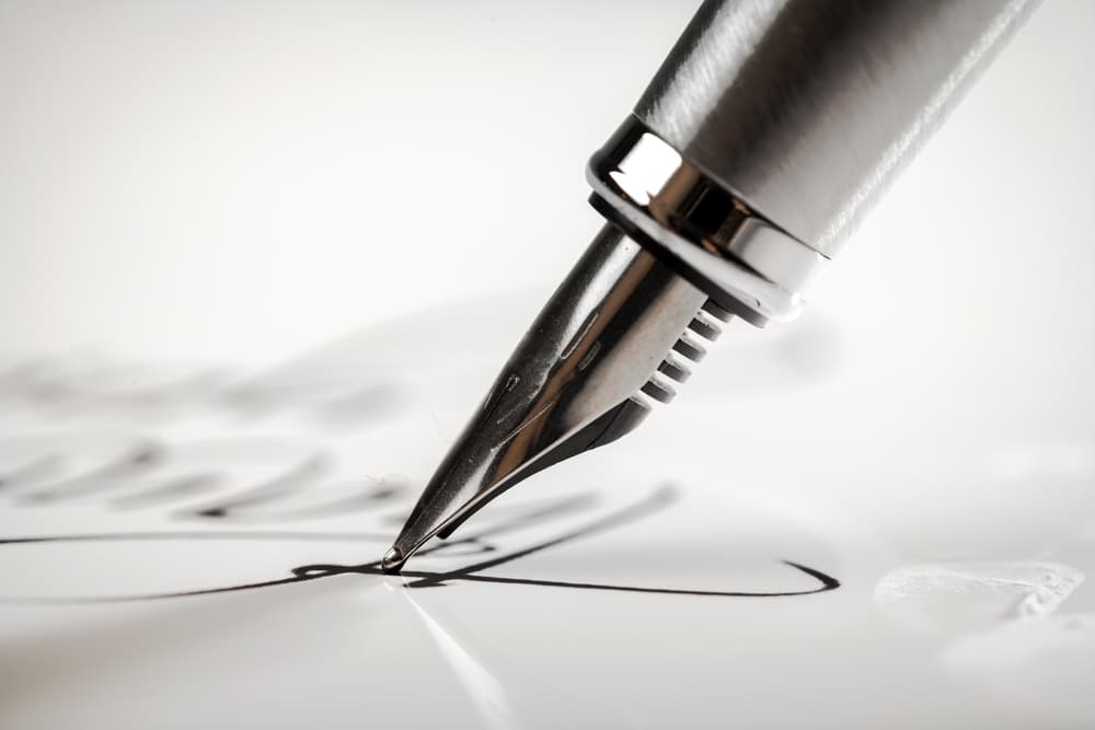 A black and white image of the head of a fountain pen writing in cursive on a piece of paper.