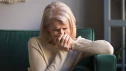 Blonde woman holding her hands over her mouth in grief.