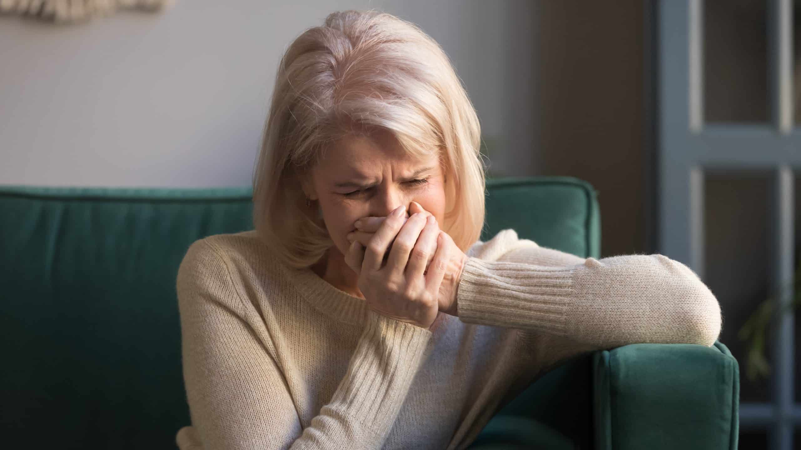 Blonde woman holding her hands over her mouth in grief.