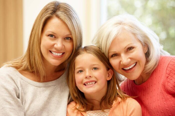Grandmother, mother, and young daughter smiling cheek to cheek, three generations of women together