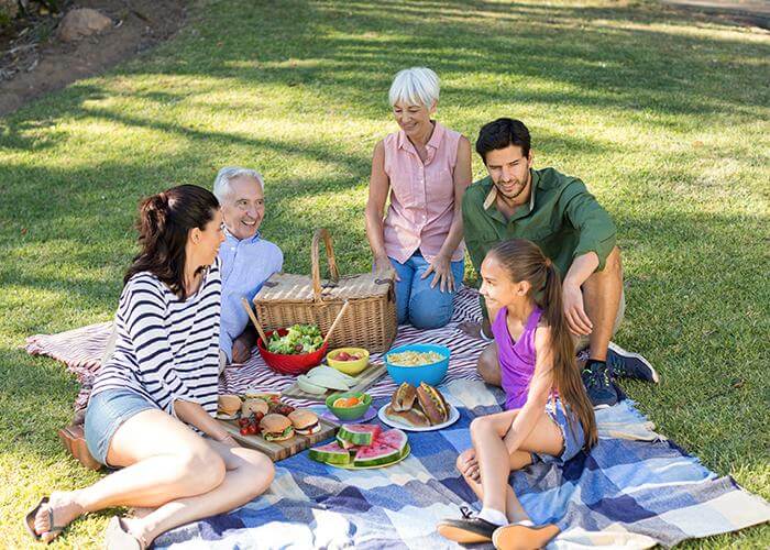 Three generations of a family sharing a picnic on a blanket in a sunny park